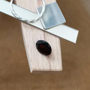 The dark red garnet oval displayed on a jewellers bench peg with some sterling silver sheet and wire.