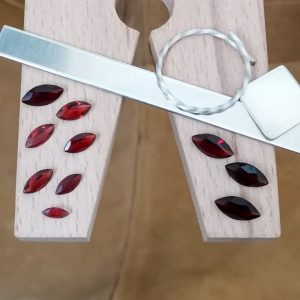 The bundle of 10 red garnet marquise gems displayed on a jewellers bench peg with some sterling silver sheet and wire.