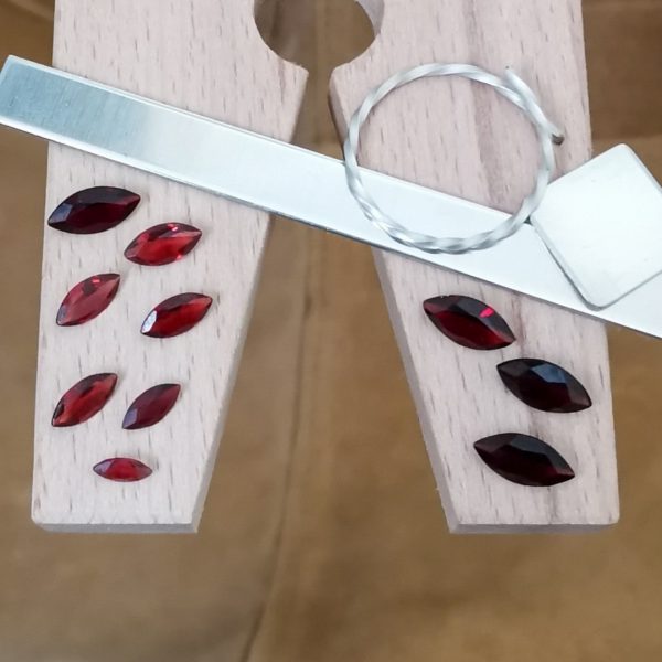 The bundle of 10 red garnet marquise gems displayed on a jewellers bench peg with some sterling silver sheet and wire.