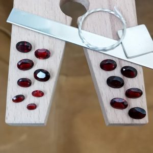The bundle of 14 red garnet ovals displayed on a jewellers bench peg with some sterling silver sheet and wire.