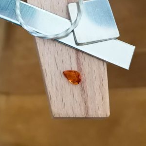 The orange hessonite garnet teardrop is displayed on a jewellers bench peg with some sterling silver sheet and wire.