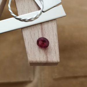 The loose dark pink garnet oval displayed on a jewellers bench peg with some sterling silver sheet and wire.