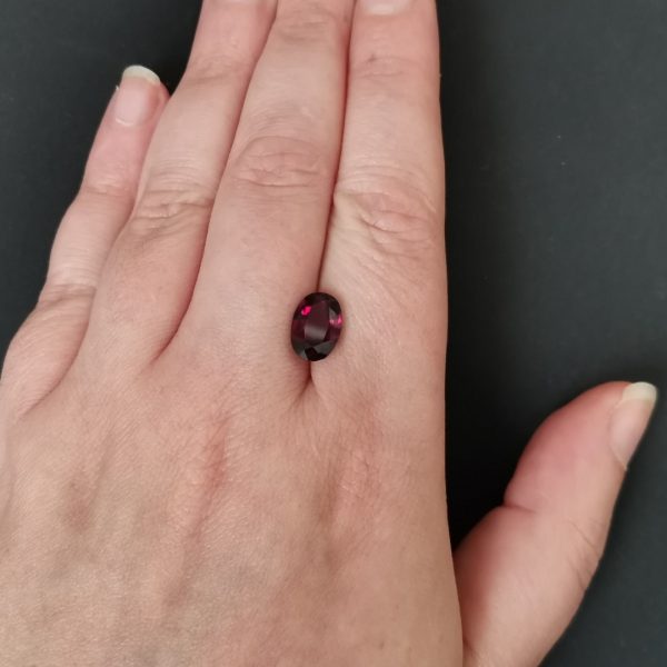 The purple garnet gemstone resting on a hand to give an idea of the gemstone size and colour.