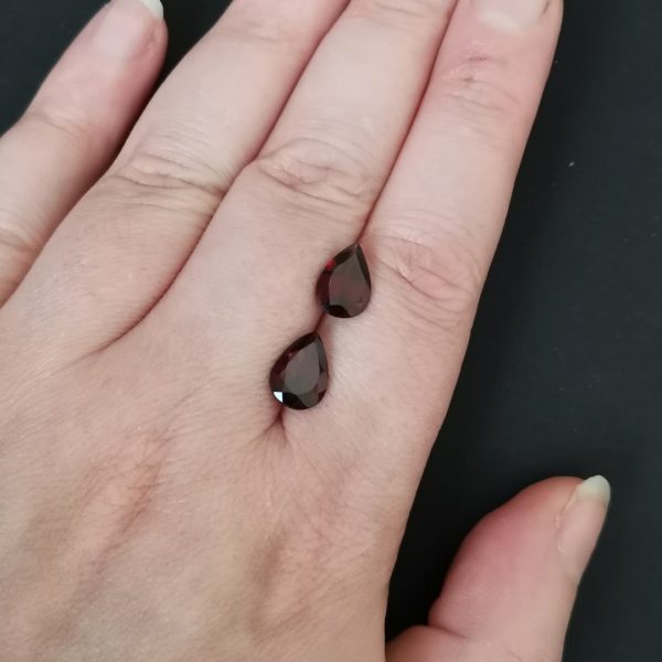 The pair of red garnet gemstones resting on a hand to give an idea of the gemstones size and colour.