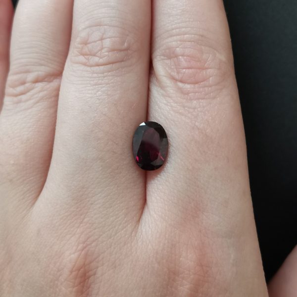 The red-purple garnet gemstone resting on a hand to give an idea of the gemstone size and colour.