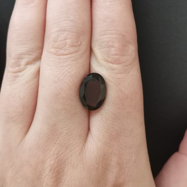 The red garnet gemstone resting on a hand to give an idea of the gemstone size and colour.