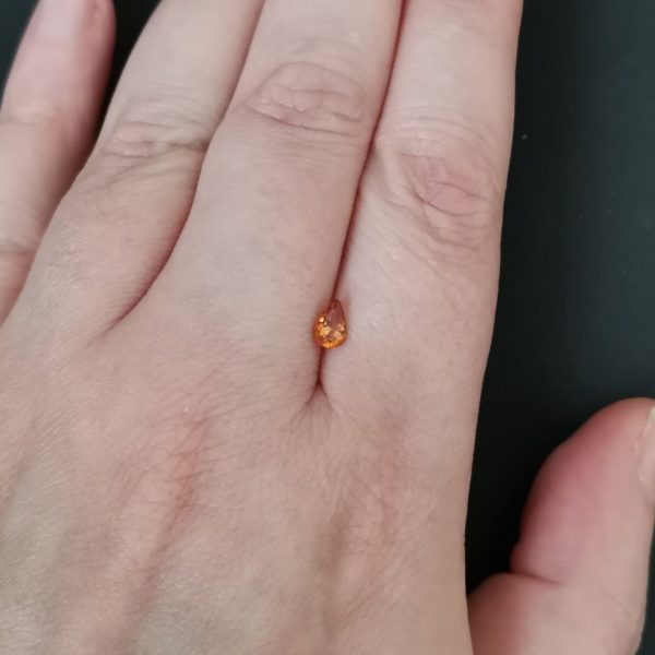 The orange garnet gemstone resting on a hand to give an idea of the gemstones size and colour.