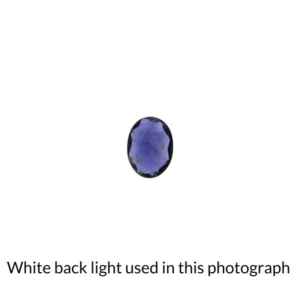 The violet iolite oval gem is being back-lit with a bright white light to show any inclusions within the gem more clearly.