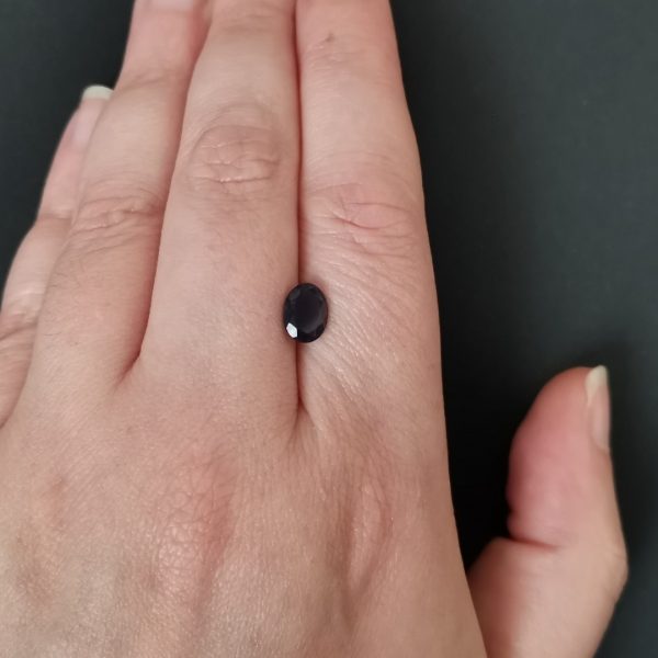 The bluish purple iolite gemstone resting on a hand to give an idea of the gemstone size and colour.