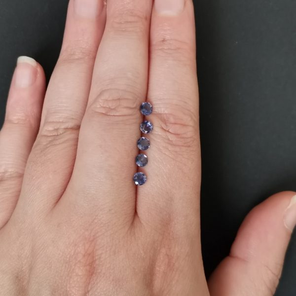 The bundle of iolite gemstones resting on a hand to give an idea of the gemstone size and colour.