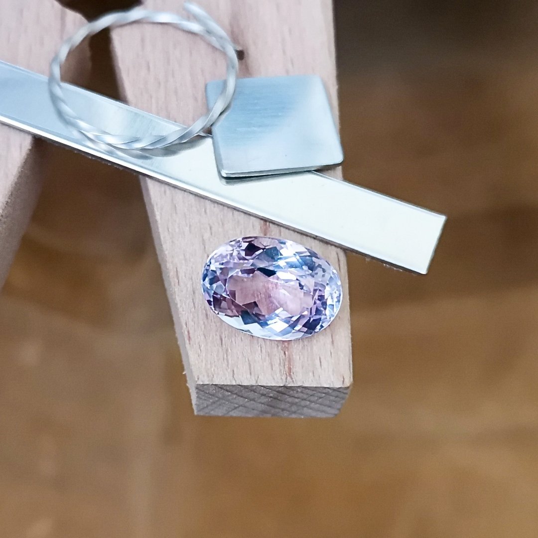 The pale pink kunzite oval displayed on a jewellers bench peg with some sterling silver sheet and wire.