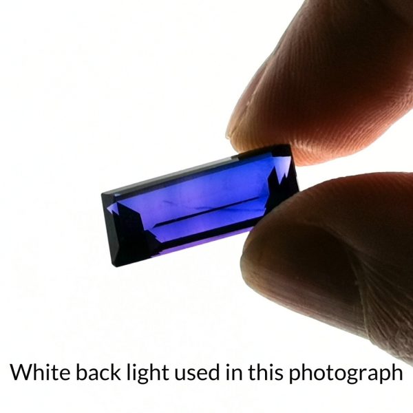 The purple lab grown sapphire rectangle gem is being back-lit with a bright white light to show any inclusions within the gem more clearly.