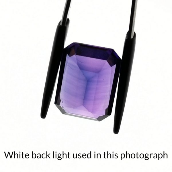 The purple lab grown sapphire rectangle gem is being back-lit with a bright white light to show any inclusions within the gem more clearly.