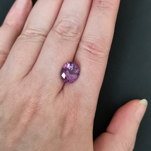 The purple lab grown sapphire gemstone resting on a hand to give an idea of the gemstones size and colour.
