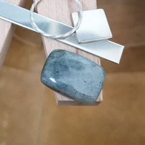The grey labradorite cabochon displayed on a jewellers bench peg with some sterling silver sheet and wire.