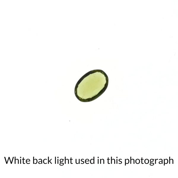 The green peridot oval gem is being back-lit with a bright white light to show any inclusions within the gem more clearly.