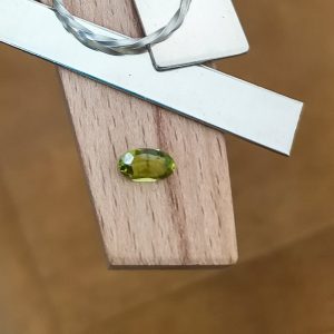 The green peridot oval displayed on a jewellers bench peg with some sterling silver sheet and wire.