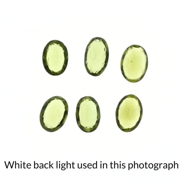 The green peridot oval gems are being back-lit with a bright white light to show any inclusions within the gem more clearly.