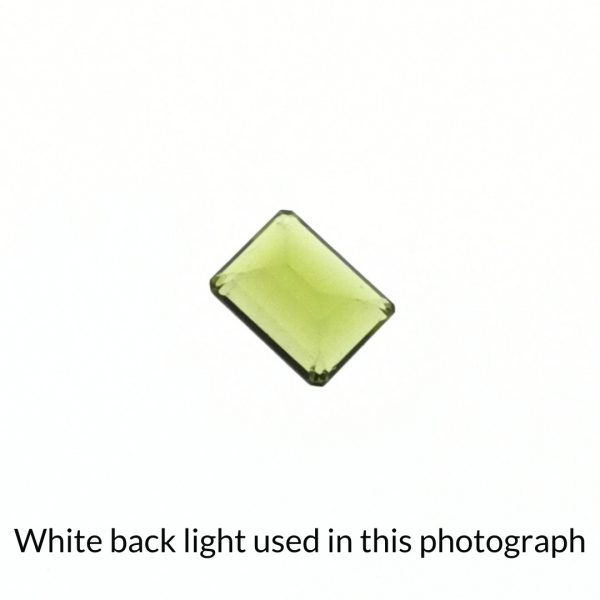 The yellow-green peridot rectangle gem is being back-lit with a bright white light to show any inclusions within the gem more clearly.