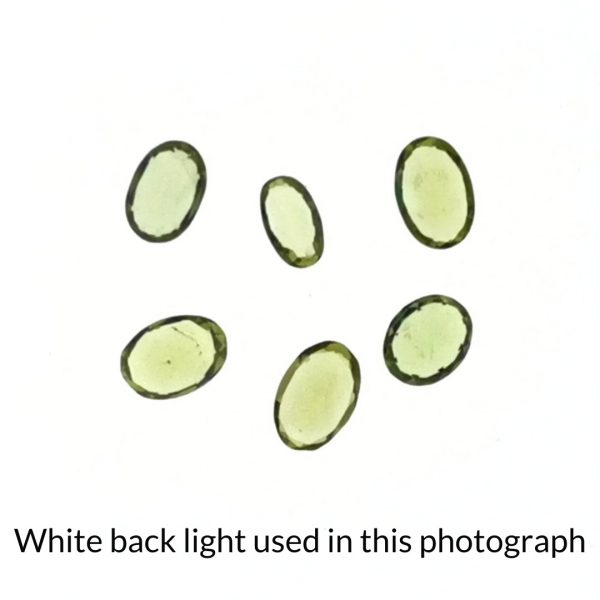 The bundle of green peridot oval gems is being back-lit with a bright white light to show any inclusions within the gems more clearly.