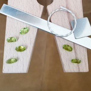 The green peridot ovals displayed on a jewellers bench peg with some sterling silver sheet and wire.
