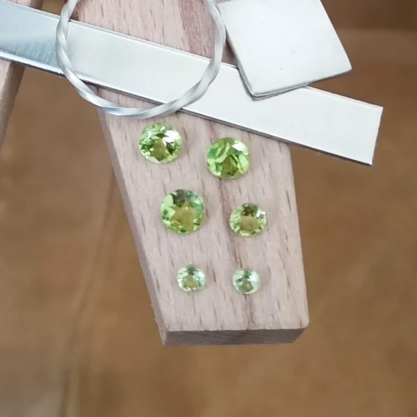 The bundle of 6 round peridots displayed on a jewellers bench peg with some sterling silver sheet and wire.