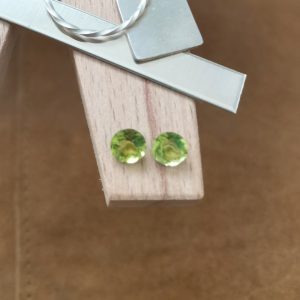 The pair of green peridot rounds displayed on a jewellers bench peg with some sterling silver sheet and wire.