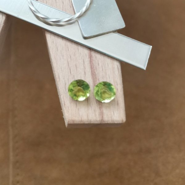 The pair of green peridot rounds displayed on a jewellers bench peg with some sterling silver sheet and wire.