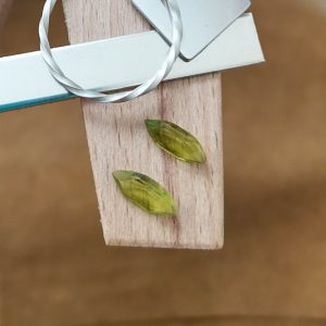 The pair of peridot marquise gems displayed on a jewellers bench peg with some sterling silver sheet and wire.