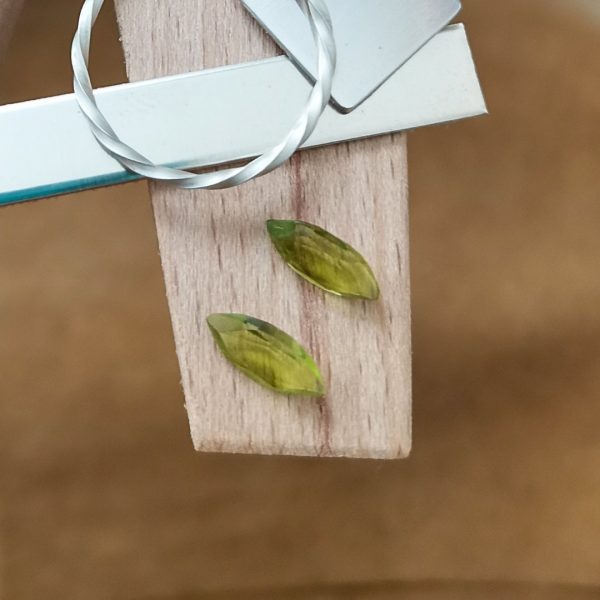 The pair of peridot marquise gems displayed on a jewellers bench peg with some sterling silver sheet and wire.