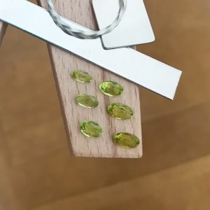 The bundle of green peridot ovals displayed on a jewellers bench peg with some sterling silver sheet and wire.