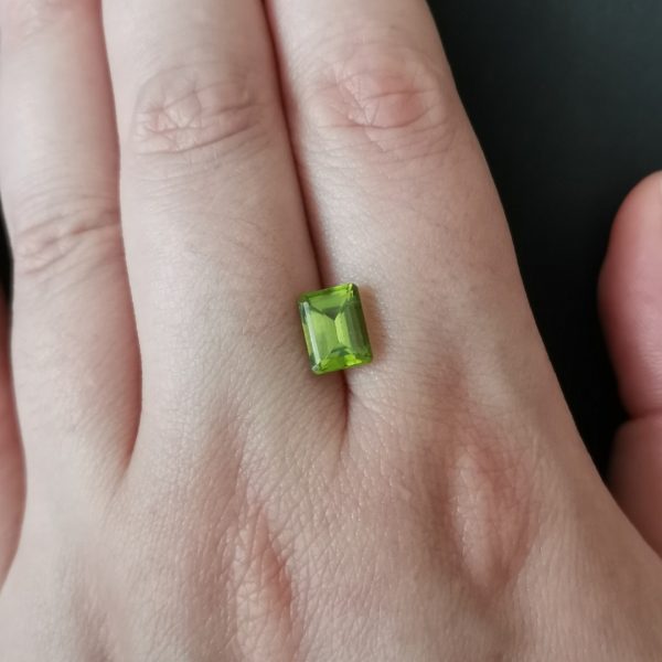 The green peridot gemstone resting on a hand to give an idea of the gemstone size and colour.