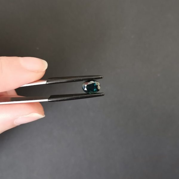A photo of the crown area of the deep teal green sapphire against a black background