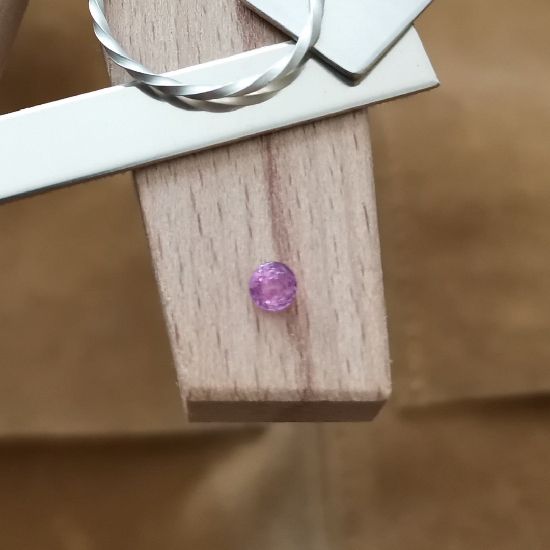 The pink sapphire round displayed on a jewellers bench peg with some sterling silver sheet and wire.