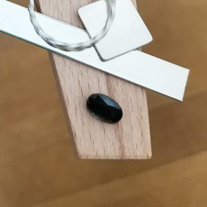 The deep green sapphire oval displayed on a jewellers bench peg with some sterling silver sheet and wire.