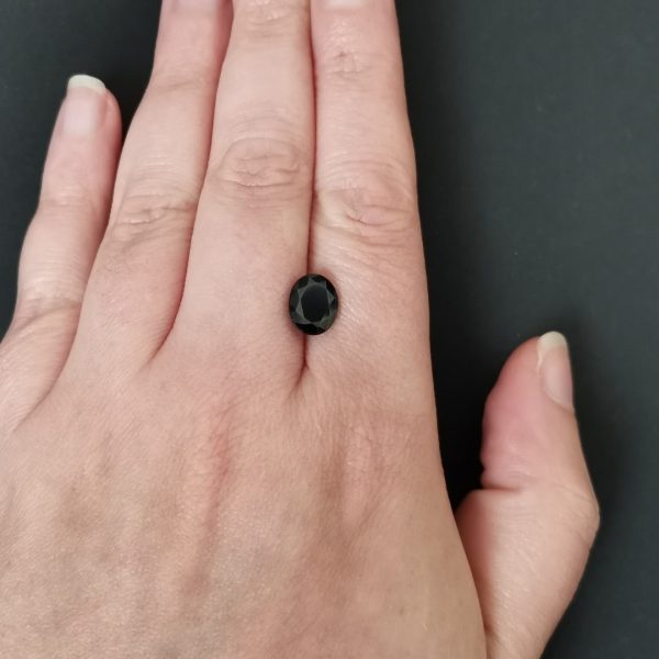 The dark blue sapphire gemstone resting on a hand to give an idea of the gemstone size and colour.
