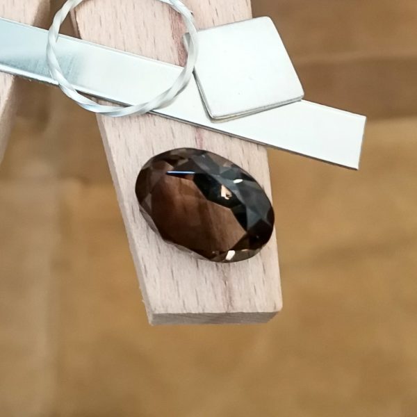 The brown smoky quartz oval displayed on a jewellers bench peg with some sterling silver sheet and wire.