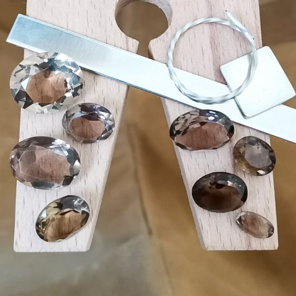 The bundle of smoky quartz ovals displayed on a jewellers bench peg with some sterling silver sheet and wire.
