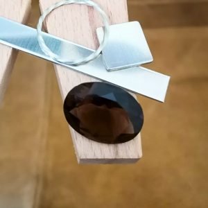 The brown smoky quartz oval displayed on a jewellers bench peg with some sterling silver sheet and wire.