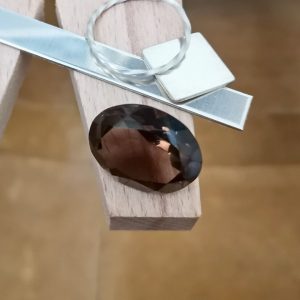 The smoky quartz oval displayed on a jewellers bench peg with some sterling silver sheet and wire.