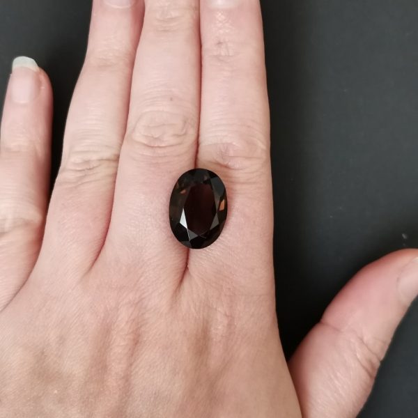 The dark brown smoky quartz gemstone resting on a hand to give an idea of the gemstones size and colour.