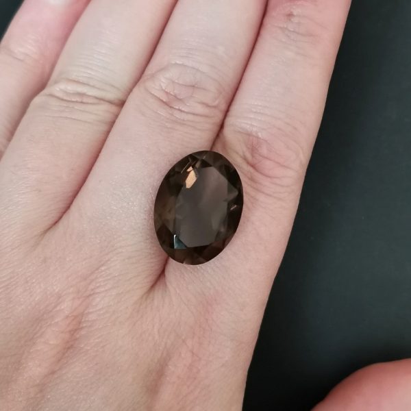 The deep brown smoky quartz gemstone resting on a hand to give an idea of the gemstones size and colour.