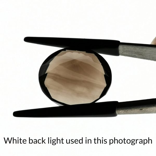 The brown smoky quartz round gem is being back-lit with a bright white light to show any inclusions within the gem more clearly.