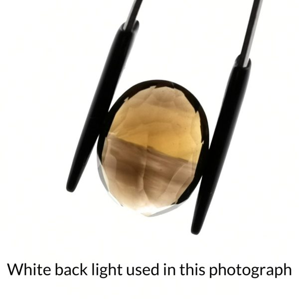 The brown and yellow smoky qyartz oval gem is being back-lit with a bright white light to show any inclusions within the gem more clearly.