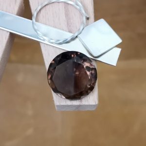 The large round smoky quartz displayed on a jewellers bench peg with some sterling silver sheet and wire.