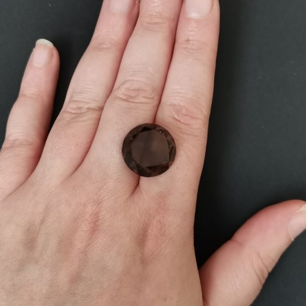 The dark brown smoky quartz gemstone resting on a hand to give an idea of the gemstone size and colour.