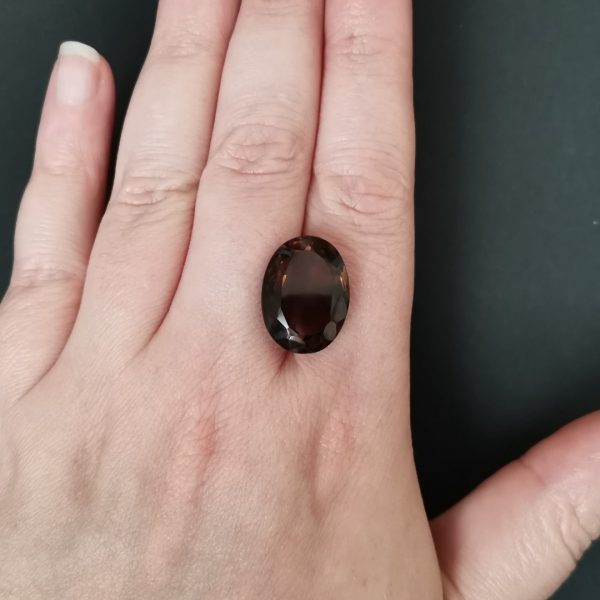 The rich brown smoky quartz gemstone resting on a hand to give an idea of the gemstone size and colour.