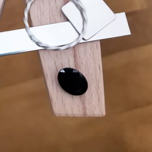 The dark blue sapphire oval displayed on a jewellers bench peg with some sterling silver sheet and wire.