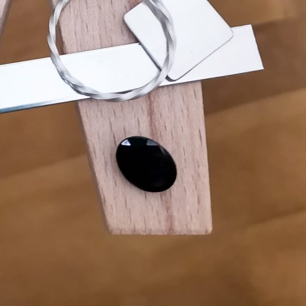The dark blue sapphire oval displayed on a jewellers bench peg with some sterling silver sheet and wire.