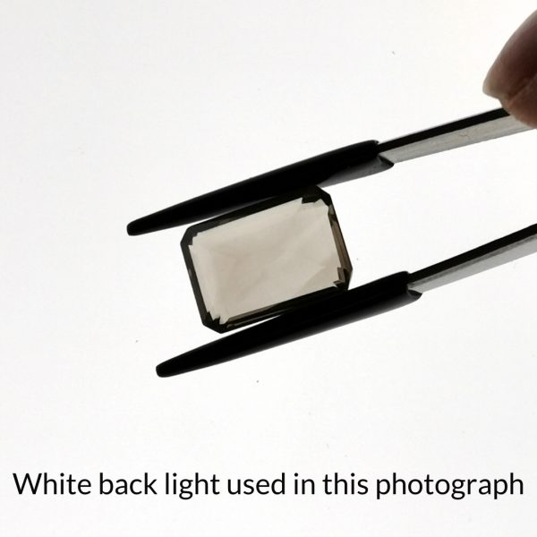 The brown smoky quartz gem is being back-lit with a bright white light to show any inclusions within the gem more clearly.
